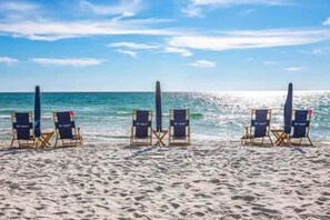 A beach with four lounge chairs and umbrellas aligned in a row.