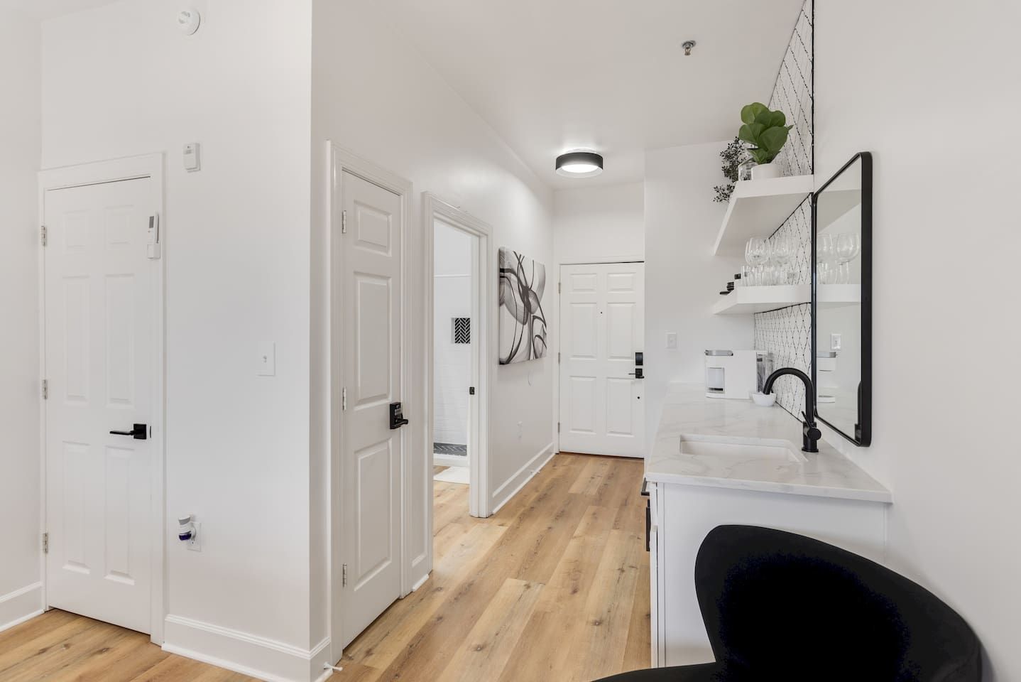 A hallway with white doors, a kitchen area with a sink and mirror, and a wooden floor.