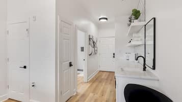 A hallway with white doors, a kitchen area with a sink and mirror, and a wooden floor.