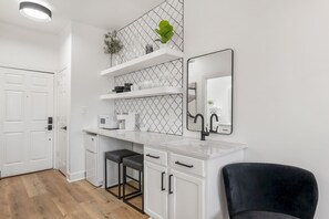A modern kitchen with white cabinetry, a marble countertop, a black chair, and a mirror.