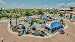 Um hotel com vários edifícios, incluindo um prédio principal com telhado azul e algumas estruturas menores. Há painéis solares nos telhados, e a área é cercada por vegetação e palmeiras.