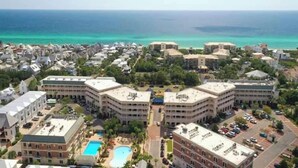Uma área costeira com vários edifícios, incluindo um hotel grande com piscina e um prédio menor com terraço no telhado.