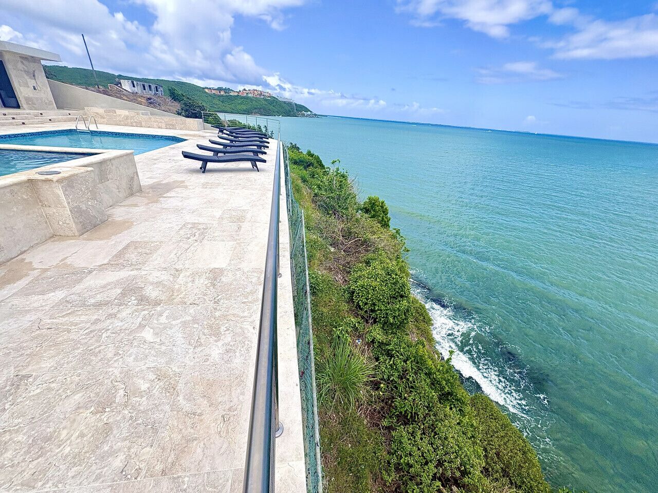 A pool area with lounge chairs overlooking a coastal view.
