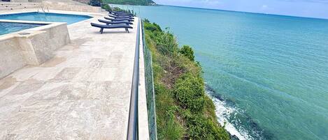 A pool area with lounge chairs overlooking a coastal view.