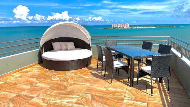 A circular outdoor seating area with a canopy, a table with chairs, and a view of the ocean and distant buildings. - Oceanfront Casa Vista Fajardo (Fajardo)