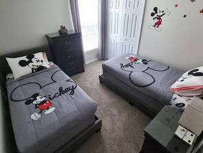 Une chambre avec deux lits, chacun agrémenté de linge de lit aux motifs de Mickey Mouse, une commode et un mur décoré d’autocollants de Mickey Mouse.