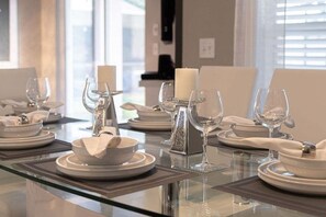 A dining table set with white plates, glasses, and a candle centerpiece.