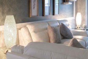 Un salon moderne avec un canapé blanc, des lampes décoratives et des œuvres d’art encadrées accrochées au mur.