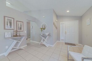 A hallway with a white reception desk, framed artwork, a potted plant, and a white door.