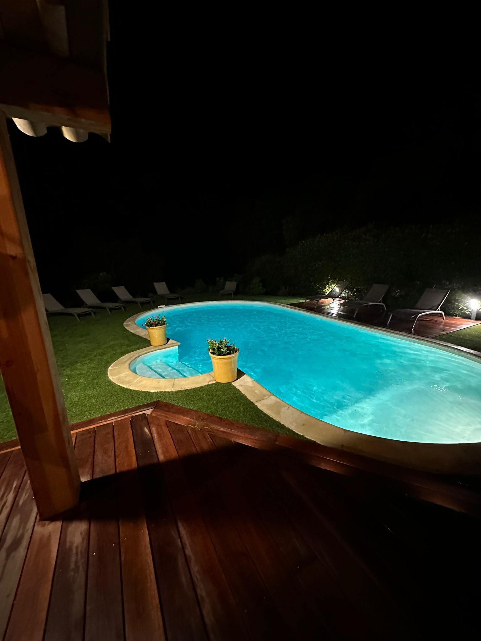 A swimming pool with a wooden deck and lounge chairs around it.