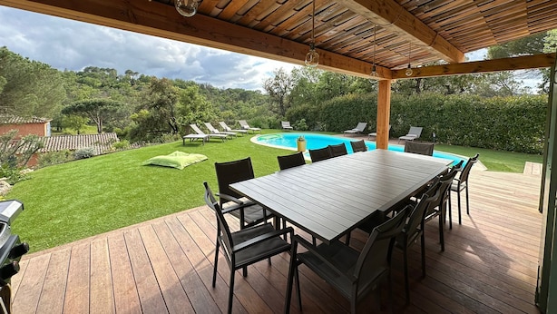 En overdækket udendørs terrasse med pool, liggestole og spisebord.