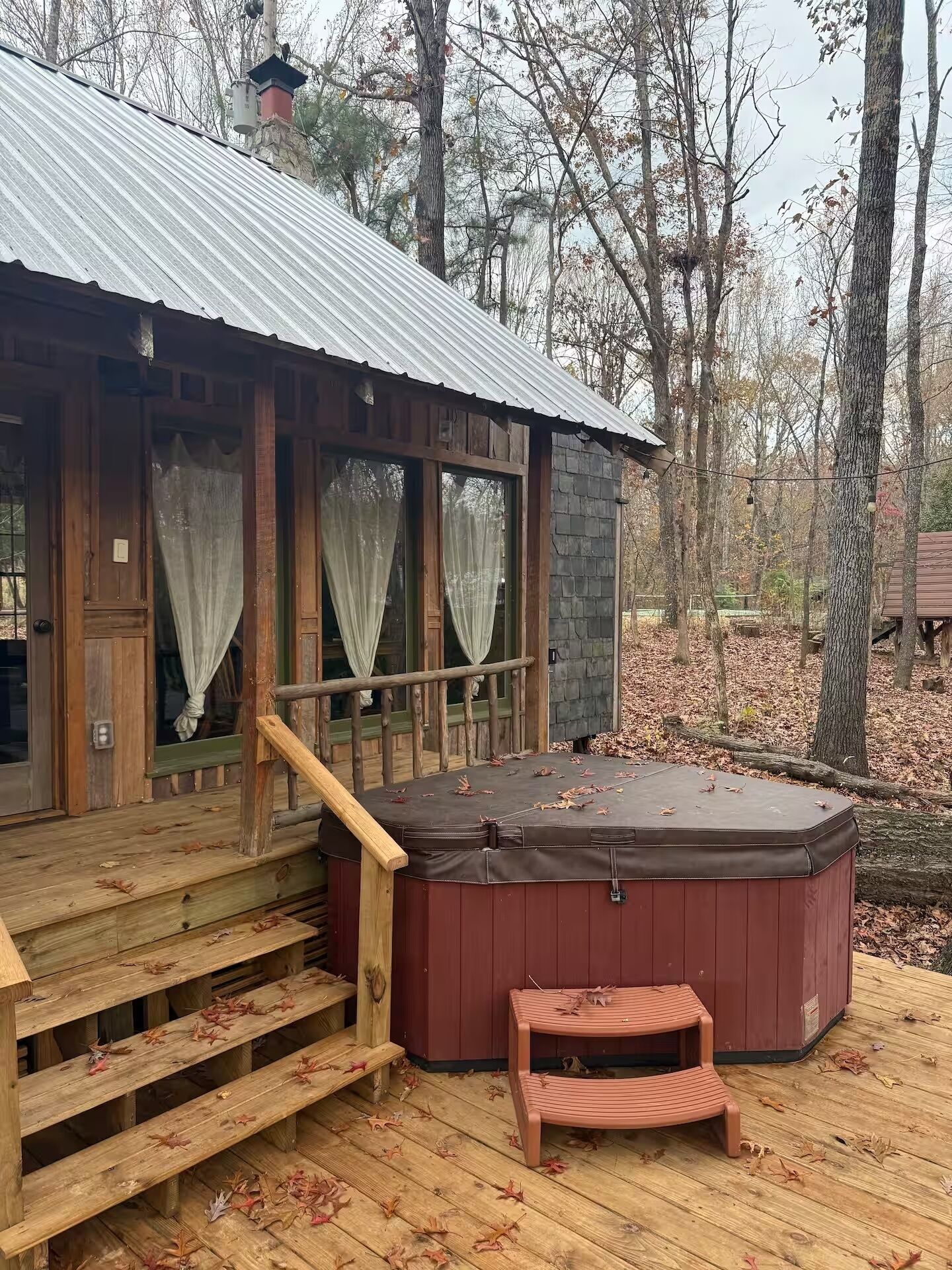 Una baita con veranda in legno, vasca idromassaggio e una scalinata che conduce all'ingresso.