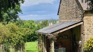 Ein Steinhaus mit geneigtem Dach, einer Veranda und einem Vorgarten.