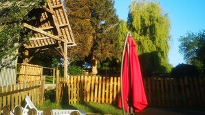 Eine hölzerne Pergola mit einem roten Sonnenschirm, umgeben von einem Holzzaun und Bäumen.