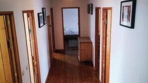Ein schmaler Korridor mit Holzboden und Holzbalkendecke. Auf beiden Seiten befinden sich Türen und eine Leuchte hängt von der Decke.