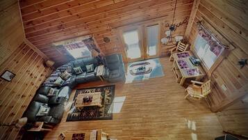 Un intérieur de chalet chaleureux avec un plafond en bois, un canapé d’angle, une table à manger et un petit coin cuisine.