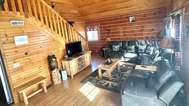 A cabin interior with a wooden floor, a staircase, a television, a sofa, and a bear-shaped decoration. - Cabin- no cleaning fees: Cranberry Fest, waterparks, trail riding for utv/atv (Warrens)