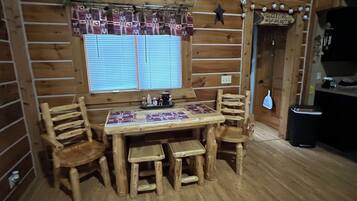 Un intérieur en bois avec une table et des chaises, une fenêtre avec des stores et une pancarte « Bienvenue ».