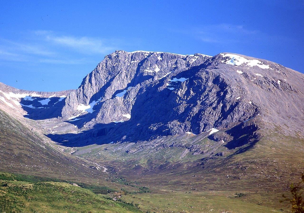 Una montaña con una pared rocosa y empinada y parches de nieve.
