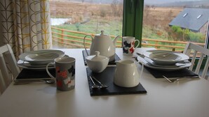 A dining table set with plates, a teapot, a mug, and cutlery, with a view of a rural landscape through a window. - Glas Beag (Spean Bridge)