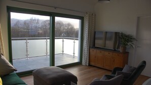 A living room with a large sliding glass door leading to a balcony, a television on a wooden cabinet, and a potted plant. - Glas Beag (Spean Bridge)