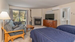 Ein Zimmer mit zwei Betten, einem Sofa, einem Fernseher, einem Kamin und einem großen Fenster.