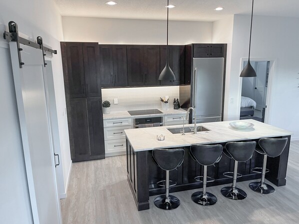 A modern kitchen with dark cabinets, a white countertop, and a bar area with four stools.
