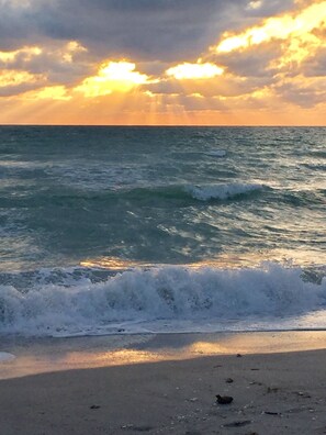 A beach with waves and a sunset in the background.