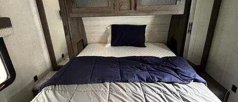 A compact bedroom with a bed, a headboard with storage compartments, and a window on one side.