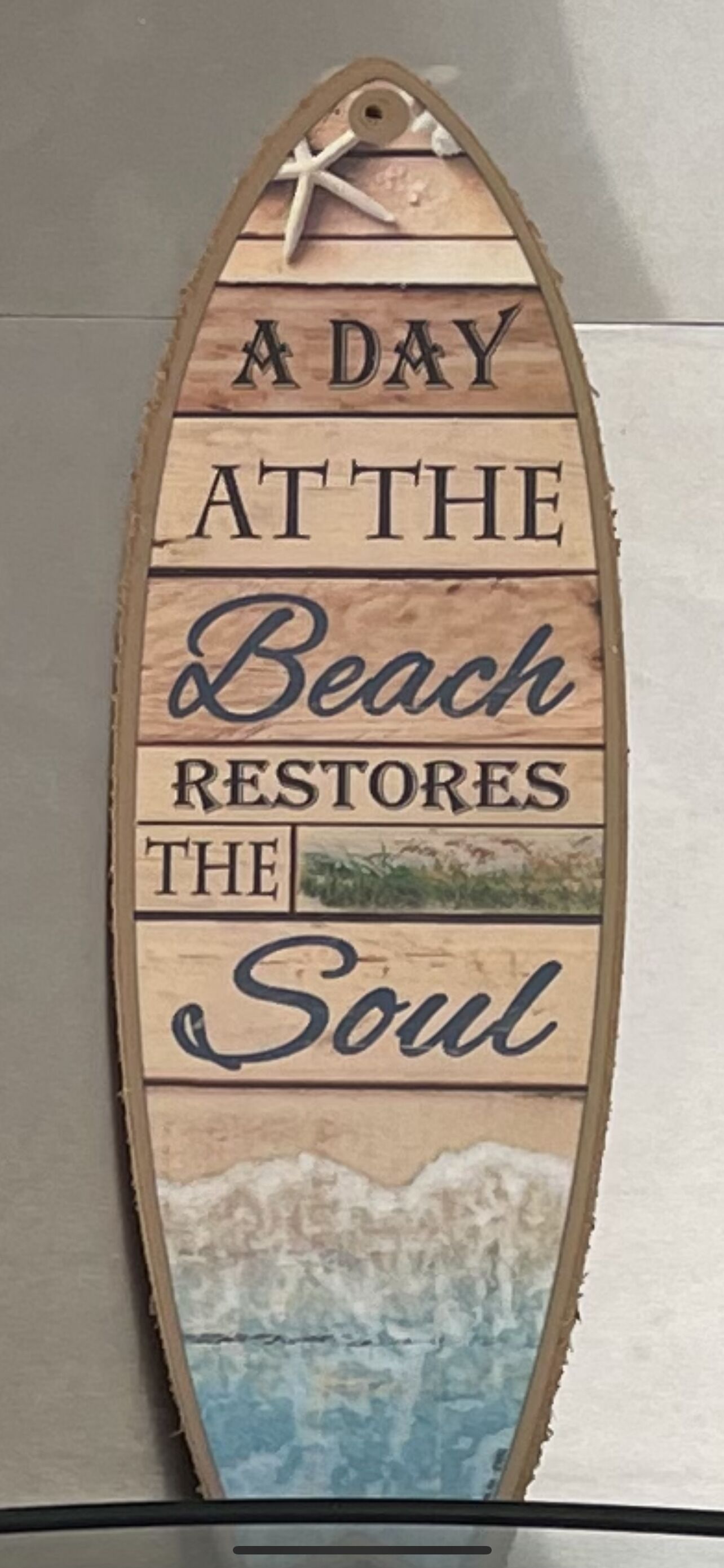 Ein Holzschild mit dem Aufdruck 'A DAY AT THE BEACH RESTORES THE SOUL' und einer Meerstern-Grafik.