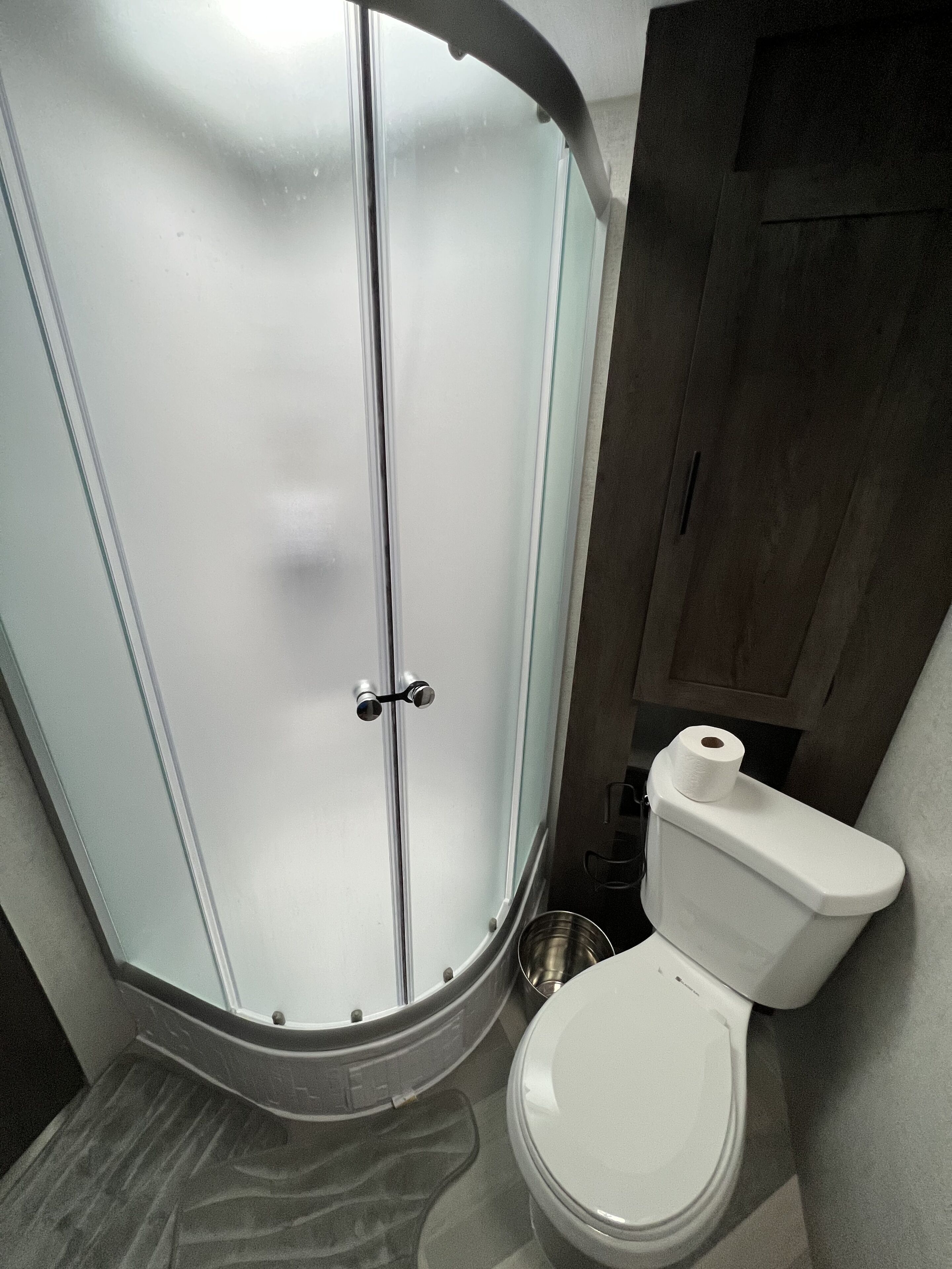 Une salle de bain avec une douche à parois de verre, des toilettes et un petit lavabo en métal.