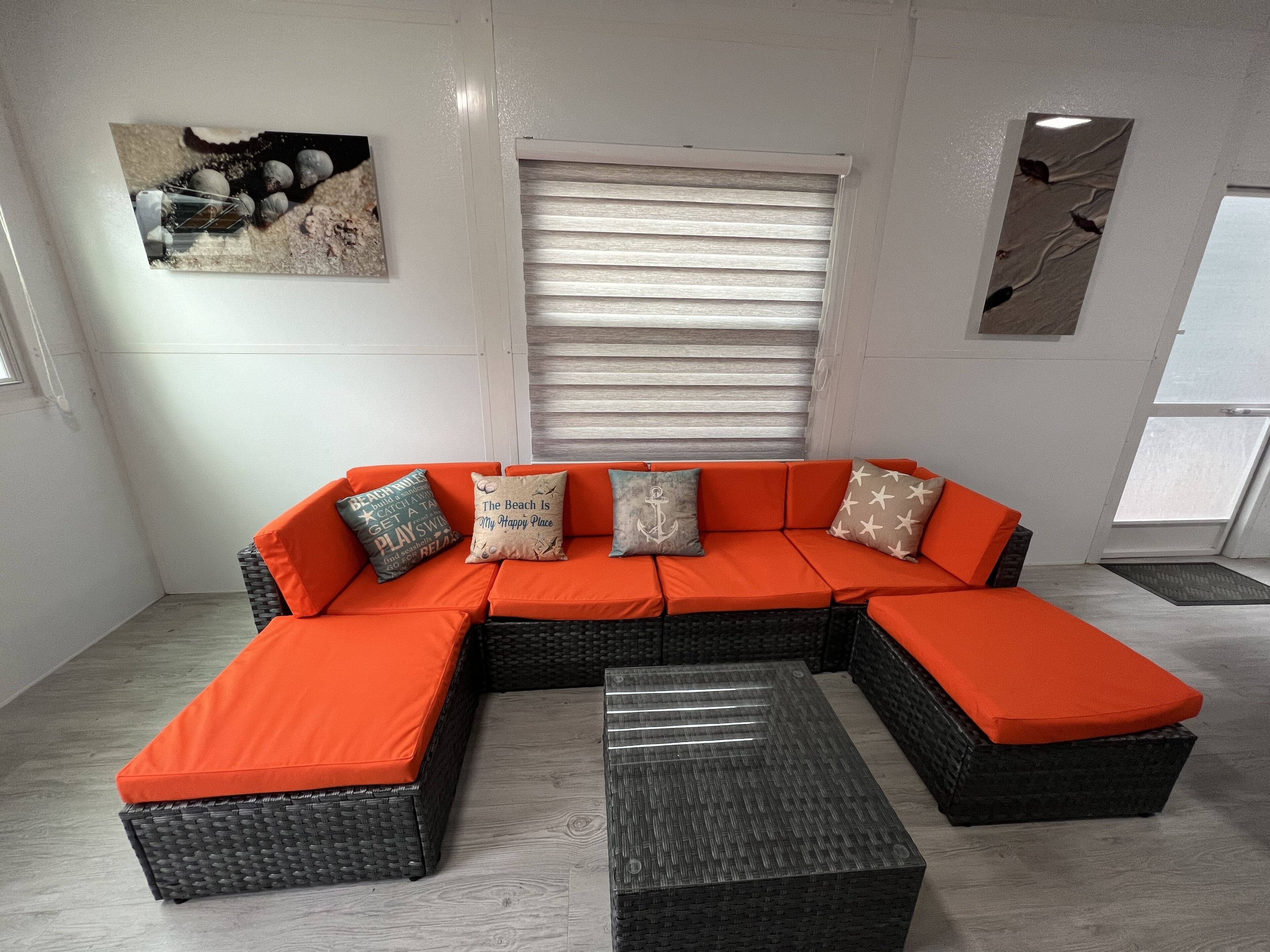 A sectional sofa with matching ottomans, a window with blinds, and a wall-mounted artwork.