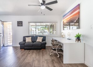 Uma sala de estar moderna com um sofá de couro preto, uma escrivaninha branca e um ventilador de teto.