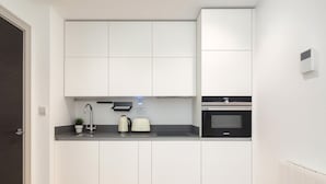 A modern kitchen with white cabinetry, a built-in oven, a kettle, and a toaster. - The Kingston Upon Thames Apartme (Kingston Upon Thames)