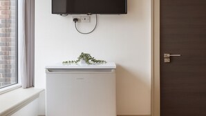 A compact refrigerator with a built-in TV above it, a small plant on top, and a wooden door to the right. - The Kingston Upon Thames Apartme (Kingston Upon Thames)