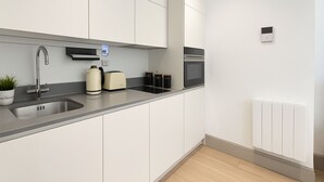A modern kitchen with a stainless steel sink, a toaster, a kettle, and a built-in oven. - The Kingston Upon Thames Apartme (Kingston Upon Thames)