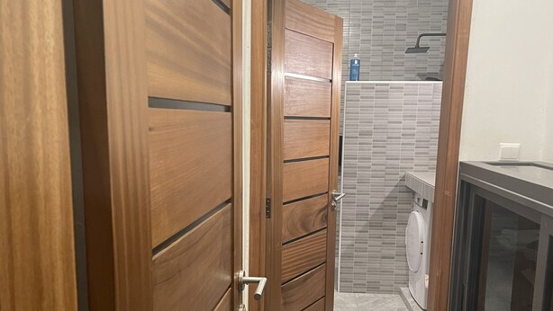 A wooden door leading to a bathroom with a tiled shower area and a washing machine.