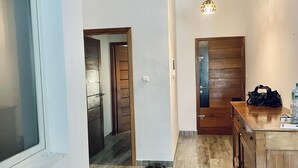 A hallway with a wooden floor, a wooden door, and a pendant light.