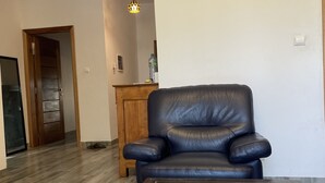 A living room with a dark leather sofa, a coffee table with a book and a remote control, and a wooden cabinet in the background.