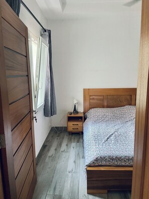 Une chambre à coucher avec un lit en bois, une table de chevet, une fenêtre avec des rideaux et une porte.