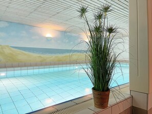 An indoor swimming pool with a view of a beach mural, a potted plant, and a tiled floor. - Appartement Unter Reet (Sylt OT Keitum)