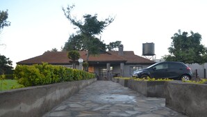 A house with a stone pathway leading to the entrance, a car parked in front, and a water tank in the background. - Burguret Kilele Guest House & Restaurant (Nanyuki)