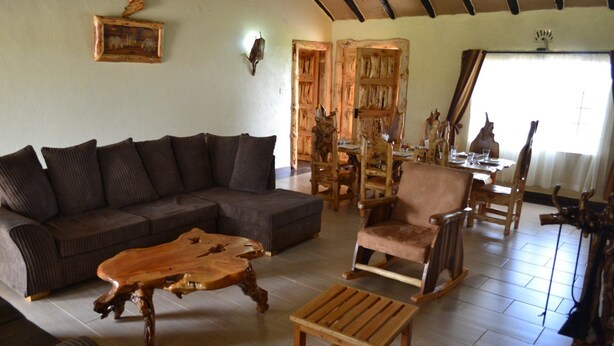 A cozy living room with a sectional sofa, a wooden coffee table, and a rocking chair. - Burguret Kilele Guest House & Restaurant (Nanyuki)