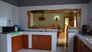 A kitchen with white tiles, wooden cabinets, a wooden-framed mirror, and a view into another room. - Burguret Kilele Guest House & Restaurant (Nanyuki)