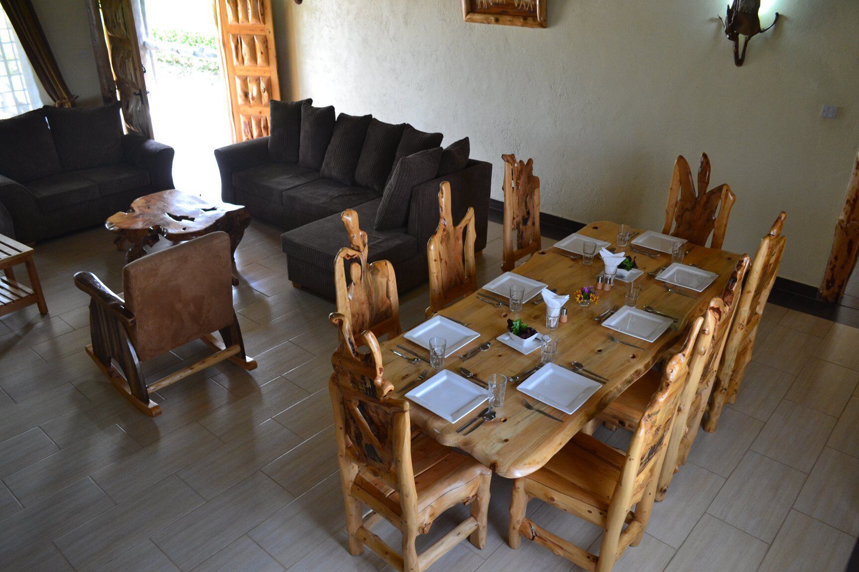 A dining area with a wooden table set for six, surrounded by wooden chairs.