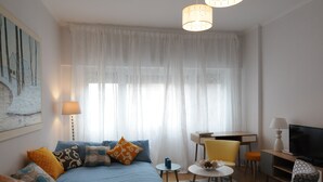 A well-lit bedroom with a bed, bedside tables, a TV, and a desk with a chair.