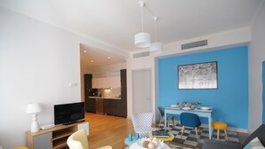 A modern living room with a TV, seating, a dining area, and a kitchen in the background.