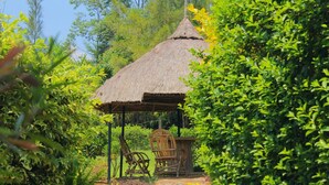 A thatched-roof structure with two wooden chairs and a table, surrounded by lush greenery. - Nguge Hills Lodge & Wellness Retreat (Nyamboyo)