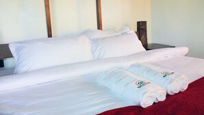 A neatly made bed with white linens and two rolled towels on a red blanket. - Nguge Hills Lodge & Wellness Retreat (Nyamboyo)