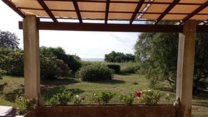 Een overdekt terras met uitzicht op een gazon en bomen.